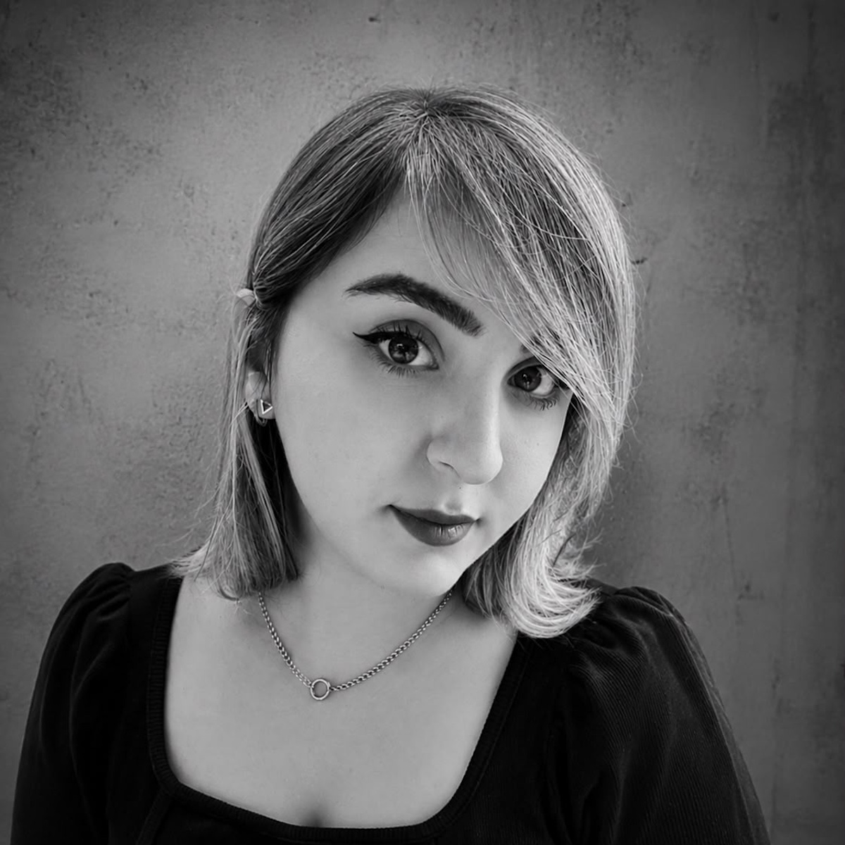 Pegah, Hairstylistin bei El Corte Hairlounge, lächelt leicht in die Kamera und trägt ein dunkles Oberteil vor einem schlichten Hintergrund.